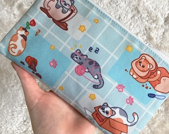 May include: A blue zippered pouch with a white zipper. The pouch has a repeating pattern of cats, stars, and paw prints. The cats are in various poses, including drinking from a cup, playing with yarn, and sitting in a box. The text "2 2" is printed on the pouch.