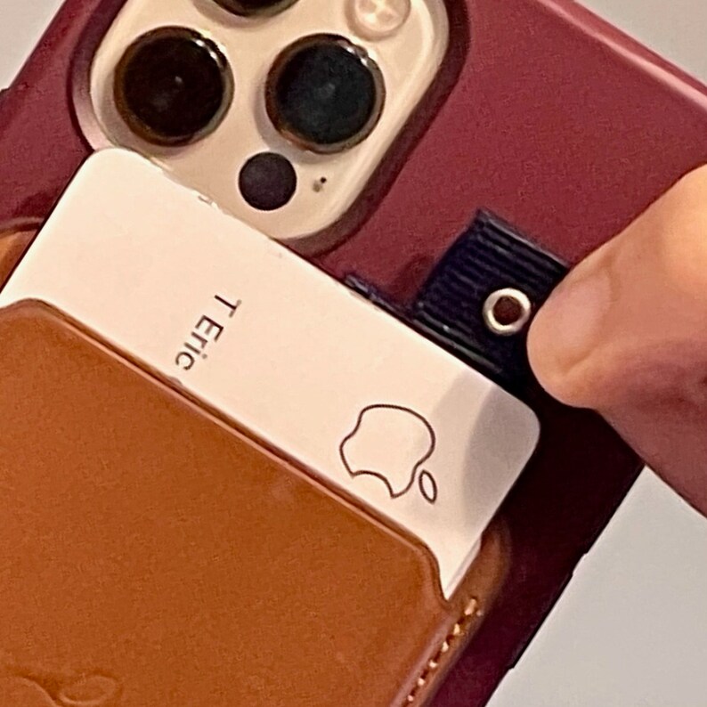 Puede incluir: Una funda de tel&eacute;fono de cuero marr&oacute;n con un porta tarjetas blanco adjunto. El porta tarjetas tiene el logotipo de Apple y el texto "T. Eric" impreso en &eacute;l.