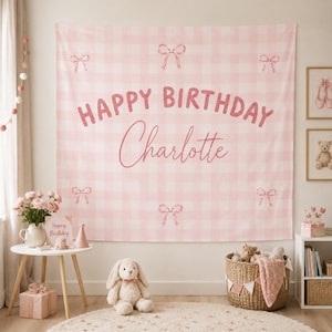 Könnte beinhalten: Ein rechteckiger Wandbehang aus Stoff mit einem hellrosa-weißen Vichy-Muster. Der Text "HAPPY BIRTHDAY" ist in fetter rosa Schrift gedruckt, darunter steht der Name "Charlotte" in kursiver rosa Schreibschrift. In den Ecken sind rosa Schleifen abgebildet.