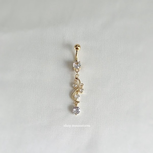 Könnte beinhalten: Goldener Körperschmuck mit einem baumelnden Anhänger in Form einer Spirale und klaren Strasssteinen. Der Anhänger ist an einem klaren Strassstein befestigt.