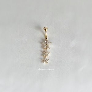 May include: Gold belly button ring with a chain of four flower-shaped charms, each with clear rhinestones. The ring is on a white background. shop moonstorm
