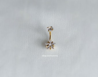 Könnte beinhalten: Goldener Körperschmuck mit einem einzelnen klaren Kristall oben und einem größeren klaren Kristallblumenmuster unten.