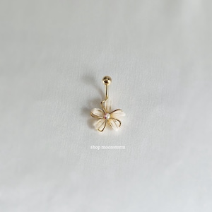 May include: Gold body piercing with a white flower charm. The flower has a small pink gem in the center.