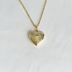 May include: A gold heart-shaped locket necklace with a delicate chain. The locket has an intricate floral design.