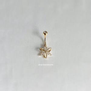 May include: Gold belly button ring with a clear crystal flower design. The ring has a small clear crystal ball at the top.