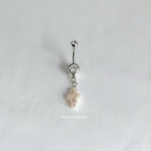 以下が含まれることがあります： クリアなクリスタルとパールクロスチャームが付いたシルバーのへそピアス