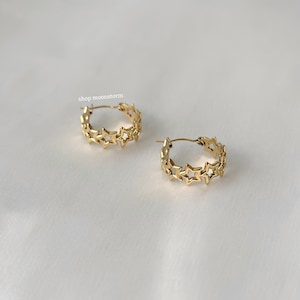 May include: Gold hoop earrings with a star design. The earrings are on a white background.