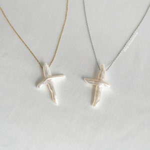 May include: Two delicate necklaces with pearl cross pendants. One necklace has a gold chain and the other has a silver chain.