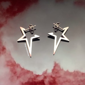 May include: A pair of silver star-shaped earrings with a simple, modern design. The earrings are made of metal and have a shiny finish.