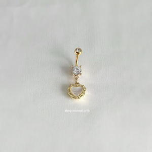 May include: Gold belly button ring with a clear crystal and a heart-shaped charm with a white center.