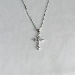 May include: A silver chain necklace with a small, silver cross pendant encrusted with clear cubic zirconia stones.