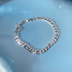 May include: A silver curb chain bracelet with a lobster clasp closure.