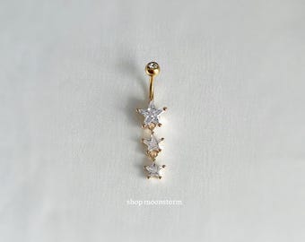 Könnte beinhalten: Goldener Bauchnabelring mit einer Kette aus fünf klaren sternförmigen Kristallen.