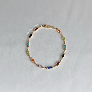May include: A gold chain bracelet featuring colourful rectangular stones. The stones are arranged in a rainbow pattern.