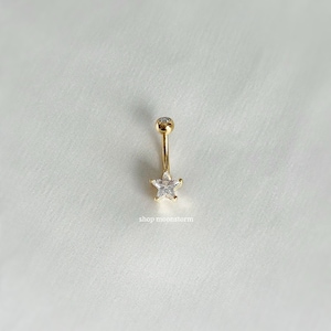 Puede incluir: Anillo de ombligo dorado con una gema transparente en forma de estrella.