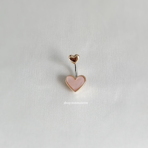 May include: A gold and pink heart shaped belly button ring with a smaller gold heart charm above the larger heart.