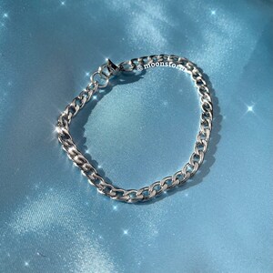 May include: A silver chain bracelet with a lobster clasp closure. The bracelet is on a blue satin background.