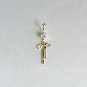 May include: Gold body piercing with a clear crystal heart and a gold bow design.  The piercing is for the belly button.