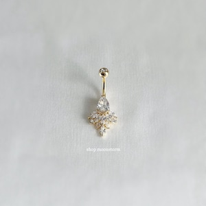 May include: Gold belly button ring with a teardrop-shaped crystal and smaller crystals surrounding it.