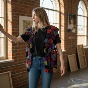 May include: A sleeveless vest constructed from numerous small, circular fabric patches in various colors including red, purple, yellow, and black. The vest is worn over a plain black short-sleeved t-shirt and blue denim jeans, featuring a textured design.