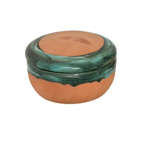 May include: A round terracotta lidded container featuring a smooth, unglazed reddish-brown base and a matching lid. The upper portion of the base and the edge of the lid are finished with a glossy, deep teal green glaze that drips downward.