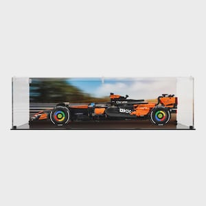 May include: A black and orange Formula 1 race car model with colourful wheel accents, displayed in a clear case. The car features the Dell and Chrome logos. The background shows a blurred image of a race track.