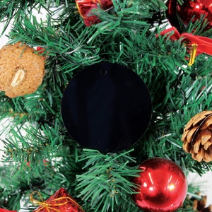 May include: A black round bauble with a hole in the centre, hanging on a green artificial Christmas tree with red and brown decorations.