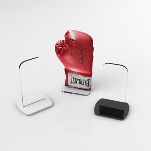 May include: A red boxing glove with a white "EVERLAST" logo and a black signature on the side. The glove is displayed on a clear acrylic stand. Two clear acrylic display stands are also shown.