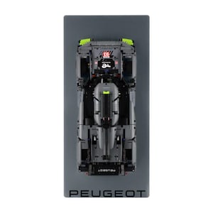 May include: A grey model race car with green detailing and the number 93 on top, presented on a grey rectangular base. The word PEUGEOT is printed in grey at the base.
