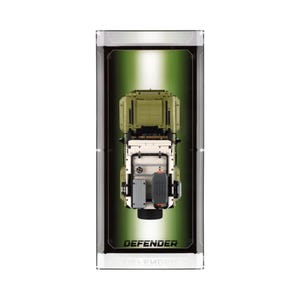 May include: A model Defender vehicle, viewed from above, presented in a display case. The vehicle is predominantly olive green and white, with black and grey accents. The display case features a green gradient backdrop, with the word "DEFENDER" printed at the base.