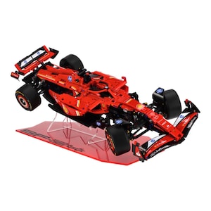 May include: A red Formula 1 race car model with black tyres and sponsor logos. The model is displayed on a red stand with the text "SF24". The car has a detailed design.