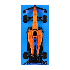 May include: Overhead shot of an orange and blue race car model on a blue surface. The model has black tyres and features the logos "webex" and "DARKTRACE". The car is a detailed replica of a Formula 1 vehicle.