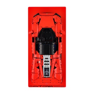 May include: A top-down view of a red model car with black detailing, set against a red background. The model car features intricate details, including a black cockpit and a detailed front end. The text "DAYTONA SP3" is visible at the bottom.