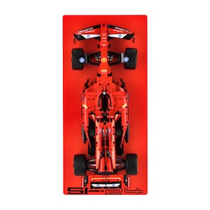 May include: A red Formula 1 race car model, viewed from above, on a red background. The model features black tyres, a detailed cockpit, and sponsor logos. The car is a detailed replica of a Formula 1 race car.
