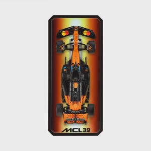 May include: A detailed model of a black and orange Formula 1 race car, viewed from above. The car's design is intricate, with visible parts. The background is a gradient of orange and yellow. The text "MCL39" is at the bottom.