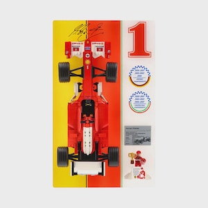 May include: A red and black toy race car with black wheels, displayed on a yellow and red background. The number 1 is on the right, with stickers and a small trophy. The car has sponsor logos.