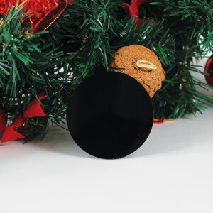 May include: A black circle bauble hanging on a green Christmas tree with red and gold decorations.
