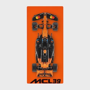 May include: A black and orange race car model, viewed from above, set against an orange backdrop. The model features black wheels and orange detailing. The text "MCL39" is visible at the bottom of the image.