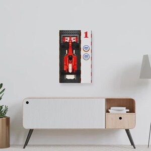 May include: A vertical canvas print depicting a red Formula 1 race car from above. The car is on a black and grey track, with the number "1" and two circular emblems on the right. The background is white, creating a striking contrast.