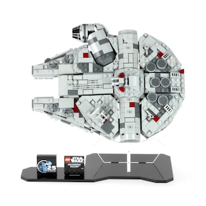 May include: A white and grey LEGO Millennium Falcon model with red accents, displayed on a black stand. The model is a 25th anniversary edition and includes a small LEGO brick with the text "LEGO Star Wars Millennium Falcon 25 Years of LEGO Star Wars".