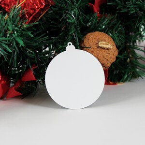 May include: A white, round, blank bauble with a silver loop for hanging. The bauble is sitting on a white surface.