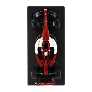 May include: A red and white Formula 1 race car model, viewed from above, is displayed on a black surface. The car has black tyres and sponsor logos. The number 24 is visible on the car's body.