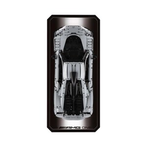May include: Overhead view of a white and black model car, AMG ONE, on a black rectangular background. The car's details are visible, including the hood, roof, and undercarriage. The AMG ONE logo is at the bottom.