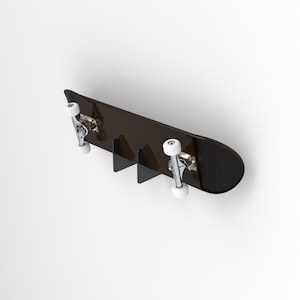 May include: A black skateboard with white wheels is mounted on a wall using a black metal wall mount. The skateboard is hanging horizontally with the wheels facing down.
