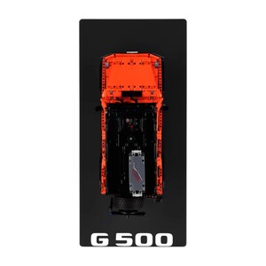 May include: Overhead view of an orange and black toy truck model on a black surface. The model has intricate details, including a visible engine and chassis. The text "G 500" is printed in white at the bottom of the black surface.