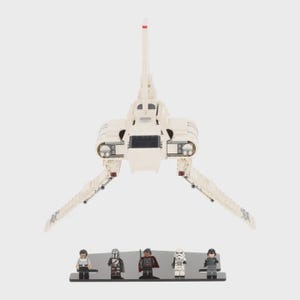 May include: A white plastic building block spaceship model with a tall central fin and two angled wings. Below the spaceship, five small plastic character figures stand on a black rectangular display base, each featuring distinct outfits and accessories.