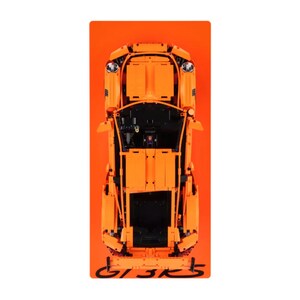 May include: An overhead view of an orange toy car model on an orange background. The car model is highly detailed, with visible components and a black interior. The text "GT3 RS" is visible in black at the bottom of the image.