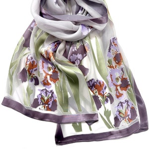May include: A white silk scarf with a floral print of purple, green and orange irises. The scarf has a purple satin trim.
