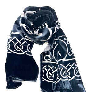 May include: A dark blue velvet scarf with a white Celtic knot design. The scarf is folded and draped over a white background.