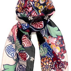 May include: A black and white silk scarf with a colourful floral and geometric pattern. The scarf is folded and tied in a knot.